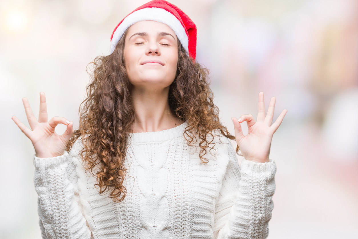 Young brunette girl wearing christmas hat over isolated background relax and smiling with eyes closed doing meditation gesture with fingers. Yoga concept.