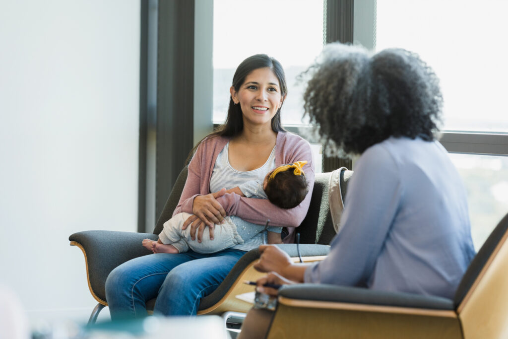 As the unrecognizable mature adult female therapist shares advice, the mid adult new mother smiles.