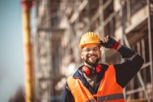 A construction worker on a work site smiles and tips their hat after overcoming depression in construction workers