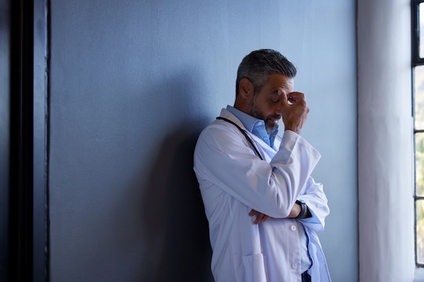 A doctor leaning against a wall with a pained expression, demonstrating depression in doctors